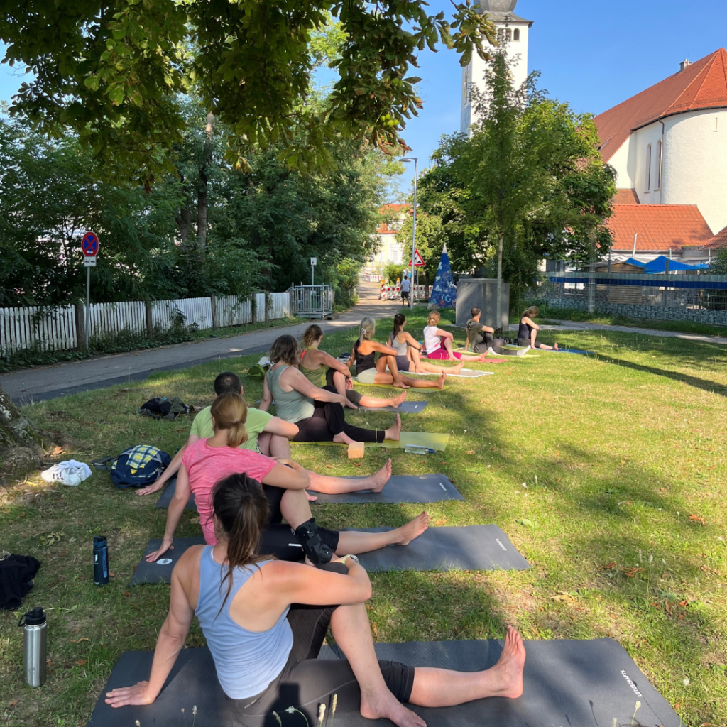 Teilnehmer*innen bei Yoga im Park bzw. Stadtpark in Bretten mit der St. Laurentiuskirche im Hintergrund. 